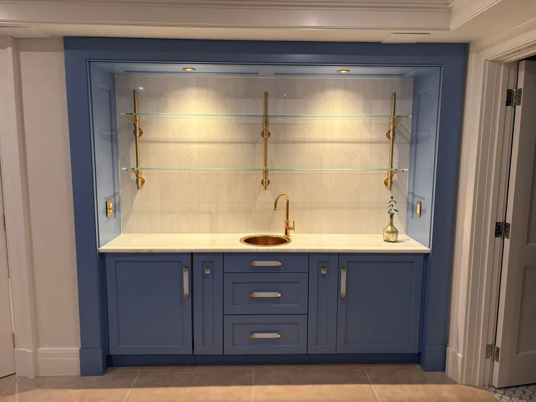 Basement wet bar with blue cabinets and glass shelving
