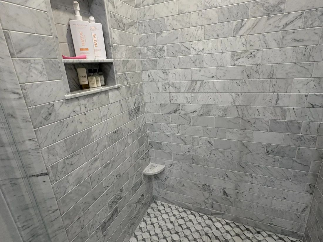 Walk-in shower with marble subway tile niche and geometric mosaic floor