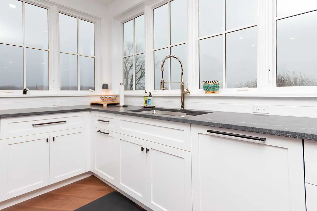 Corner view of white kitchen cabinets with windows above the sink
