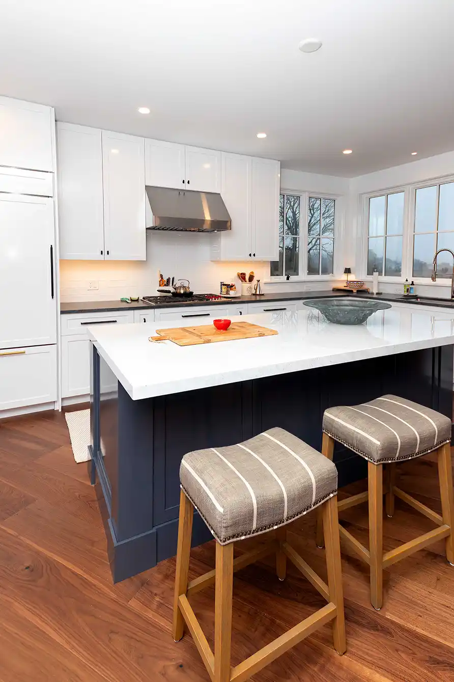 End of the navy kitchen island with two woven stools on a walnut floor